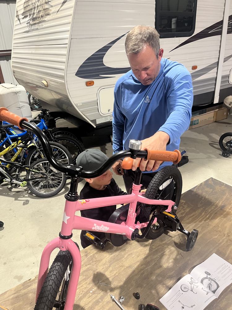 A dad and kid working on a pink bike